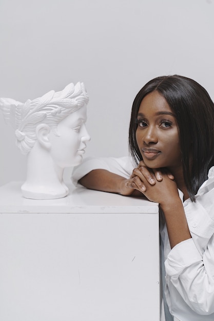 African woman in a studio. White wall.  Woman in a white shirt.