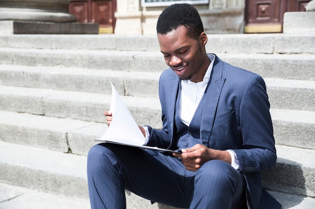 An african young businessman talking on mobile phone sitting on staircase with laptop