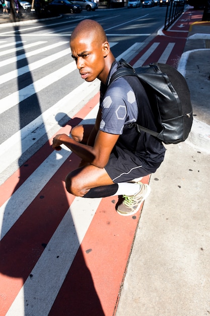 An african young male athlete crouching on roadside looking away