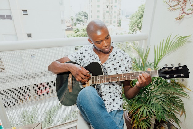 African young man playing the guitar sitting in the balcony