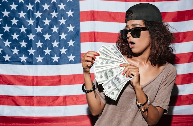 African young woman with money standing over USA flag