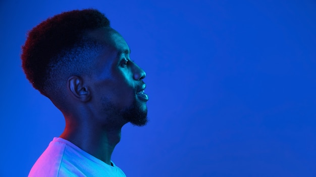 Africanamerican young mans portrait on dark studio wall in neon side view