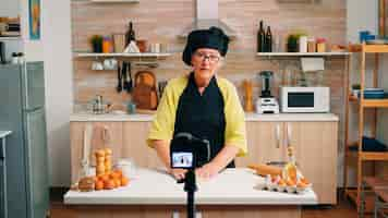 Free photo aged female vlogger making social media video about cooking for the internet channel. retired blogger chef influencer using technology communicating, shooting blogging with digital equipment