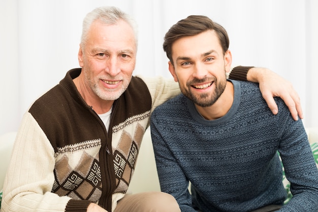 Free Photo aged happy man hugging young smiling guy on sofa