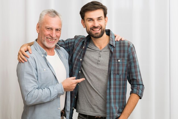 Aged happy man pointing and hugging with young smiling guy