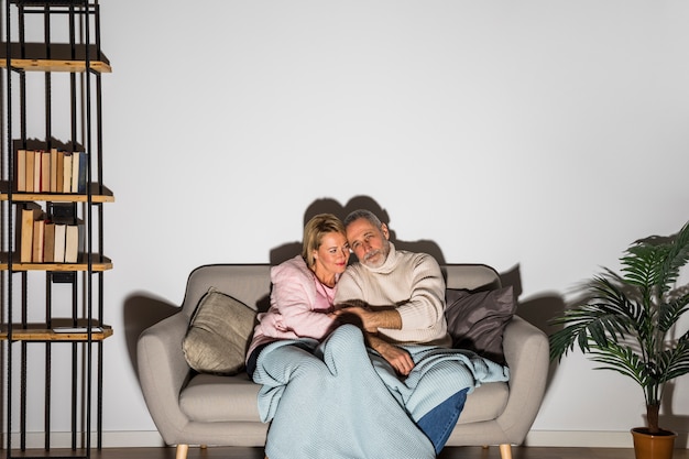 Aged man holding hands with woman and watching TV on sofa