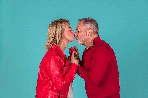 Aged man with jewellery box kissing with woman