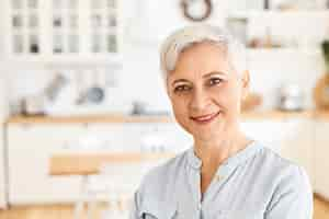 Free photo aged people, maturiry and retirement concept. charming cheerful european woman pensioner dressed in casual clothes enjoying calm morning indoors, being in good mood, waiting for son for breakfast