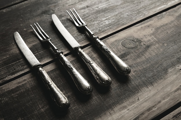 Free Photo aged retro vintage set of stainless steel forks and knives covered with patina isolated on brushed black wooden table side view