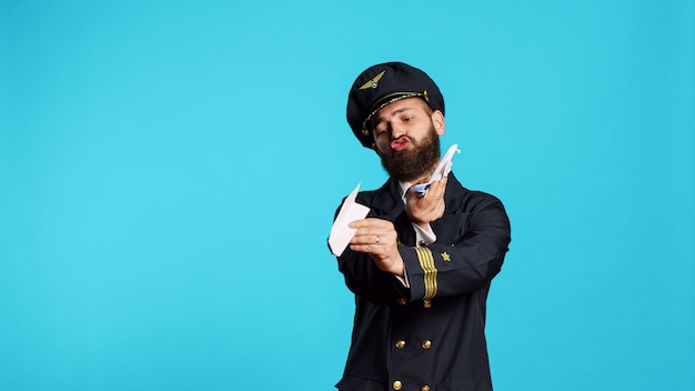 Free photo airline pilot playing with paper and mini airplane, having fun with origami and small artificial aircraft in studio. young male aviator wearing flying uniform, working on commercial flights.