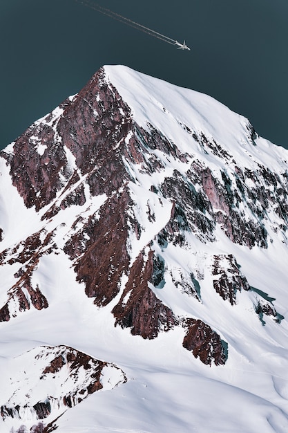 Airliner With Contrail Passing Above the Snowy Mountain Peak