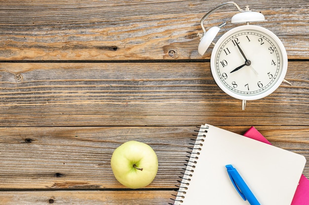 Free photo alarm clock apple and notepads on a wooden surface top view