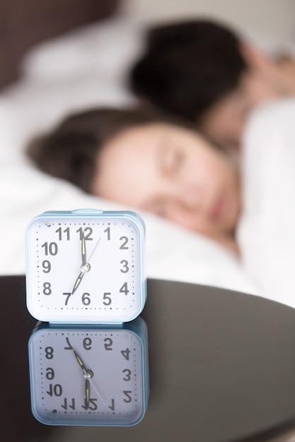 Alarm clock and couple asleep early in the morning, vertical