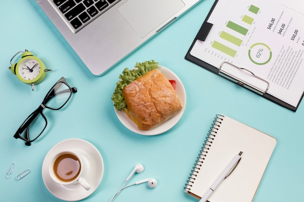 Alarm clock,eyeglasses,breakfast,earphones,spiral notepads and budget plan on clipboard against blue backdrop