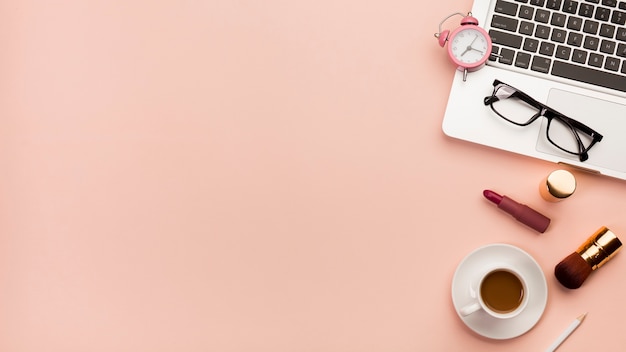 Free Photo alarm clock,eyeglasses on laptop with coffee cup and makeup product against peach backdrop