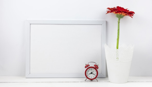 Free photo alarm clock and gerbera flower with empty frame on desk