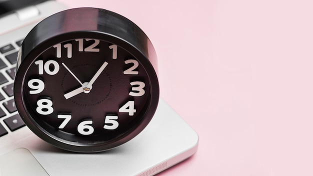 Free photo alarm clock on laptop against pink background