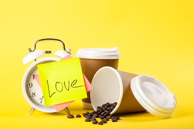 Free photo alarm clock paper cup paper reminder and coffee beans on yellow background