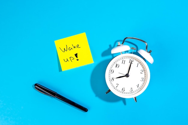 Free photo alarm clock and a sticker with the inscription wake up on a blue background