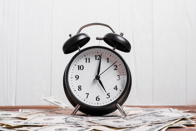 Free photo alarm clock on us dollar currency notes on wooden desk against white wall