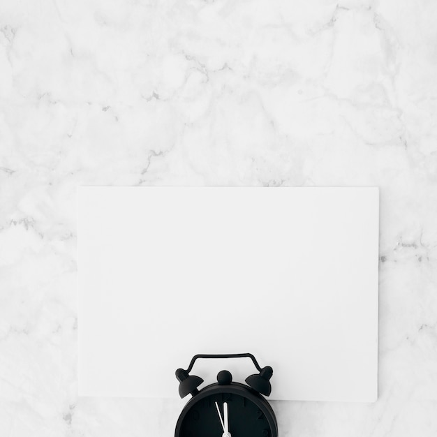 Free Photo alarm clock over the white blank paper against marble textured background