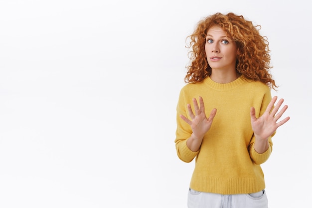 Free photo alarmed and worried curly redhead woman calm down person, saying dont shoot, raising arms, begging to stop, look freak-out or nervous, persuade someone drop gun, white wall