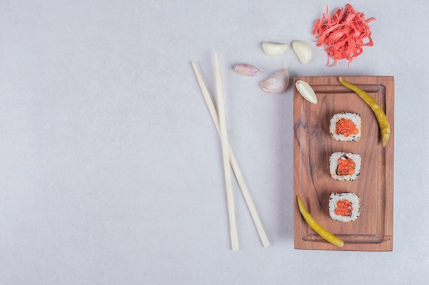 Alaska sushi rolls decorated with red caviar on white background with chopsticks and pickled ginger.