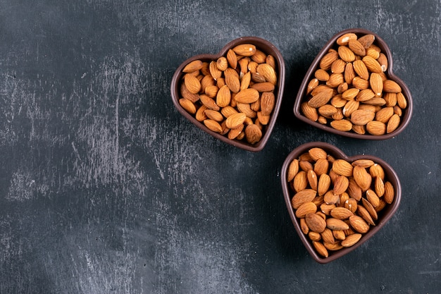 Almond in a heart shaped bowls on a black stone table. flat lay