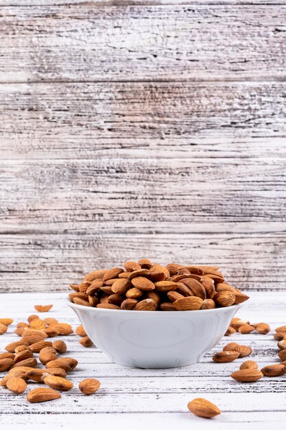 Almond in a white bowl on a white wooden table. side view.