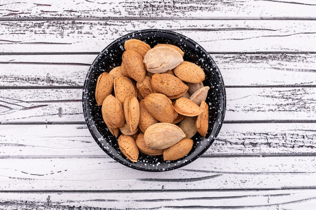 almonds in black bowl top view on white wood