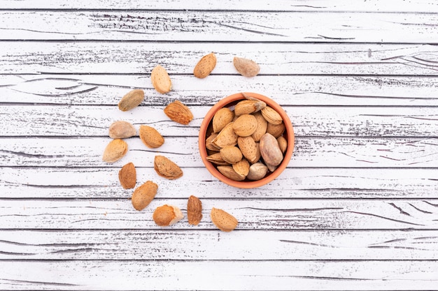 Free photo almonds in ceramic bowl near the spreaded almonds on white wooden  surface