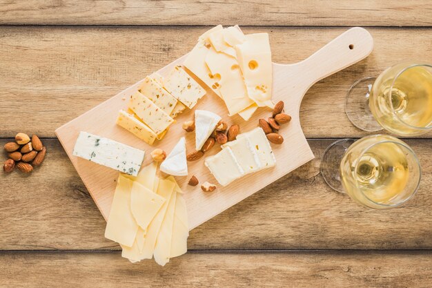 Almonds and different type of cheese with wine on wooden desk