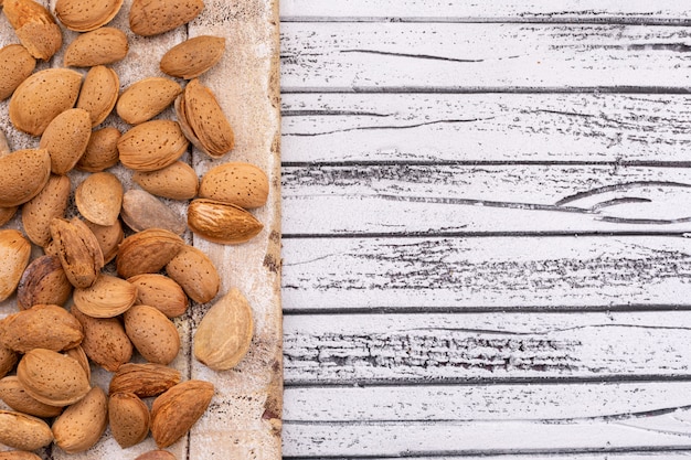 almonds on wooden texture board on the left of white wooden