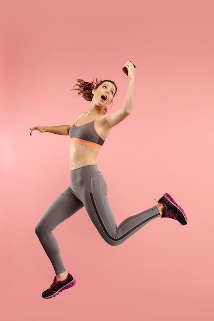 Free Photo always on mobile. full length of pretty young woman taking phone while jumping against red studio background.