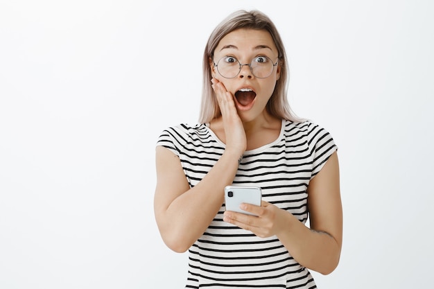 Free photo amazed and astonished blonde girl posing in the studio with her phone