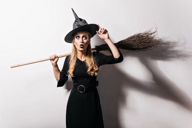 Free Photo amazed blonde witch touching her magic hat. attractive vampire girl preparing for carnival in halloween.