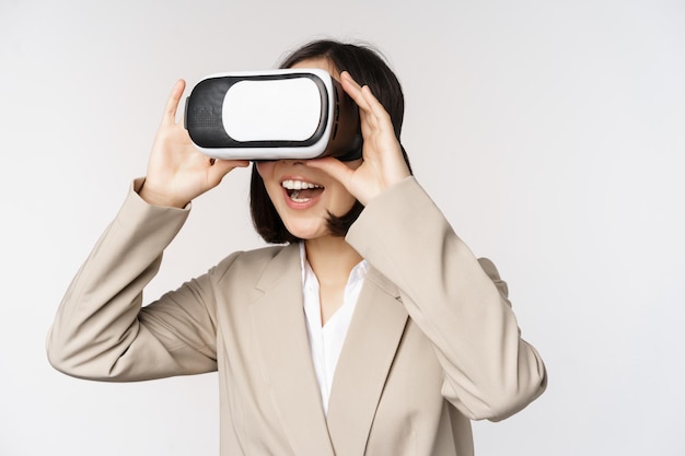 Amazed business woman in suit using virtual reality glasses looking amazed in vr headset standing over white background