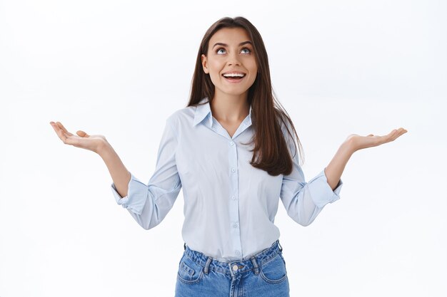 Amazed and happy cheerful woman raise hands and looking up amused as something cool falling from sky, catching money or seeing miracle, standing wondered and fascinated over white wall