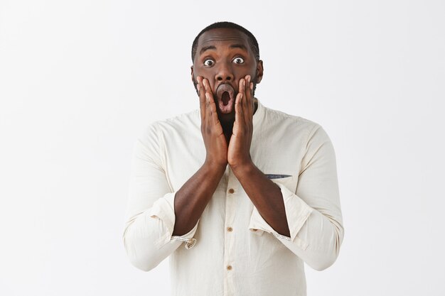 Amazed and surprised young guy posing against the white wall