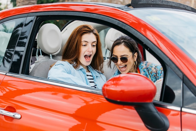 Amazed young lady and cheerful woman sitting in car