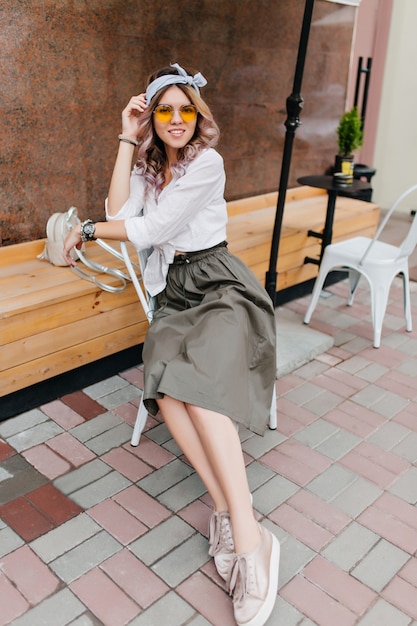 Free Photo amazing girl in classic shirt and sport shoes chilling in outdoor cafe and posing in comfortable pose