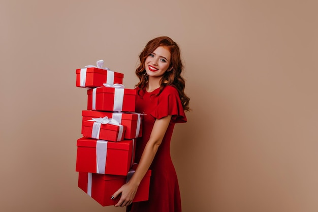 Free photo amazing girl with wavy ginger hair holding red presents studio photo of emotional female model posing with christmas gifts