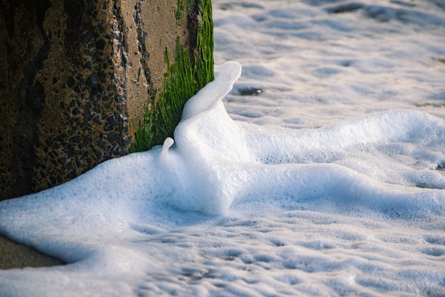 Free Photo amazing shot of sea waves hitting a stone column covered with moss and making splashes