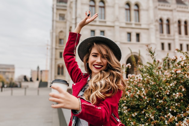 Amazing woman with long wavy hair fooling around on the street with cup of coffee