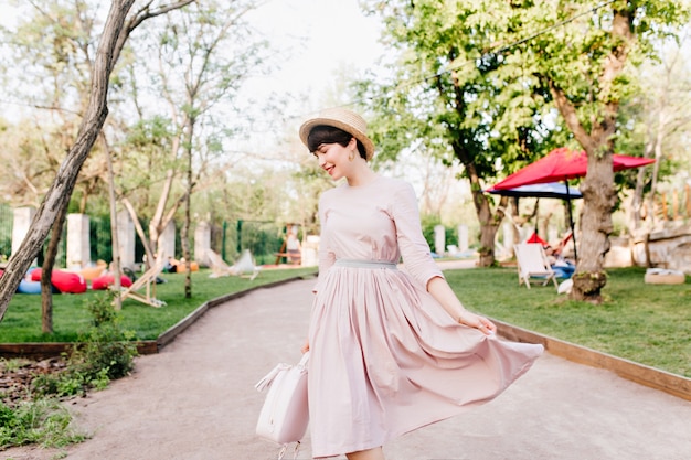 Amazing young lady playing with her long light-purple dress, walking in park alley before picnic with friends