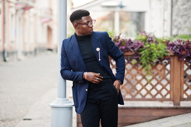 Amazingly looking african american man wear at blue blazer with brooch black turtleneck and glasses posed at street Fashionable black guy