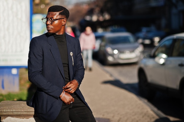 Amazingly looking african american man wear at blue blazer with brooch black turtleneck and glasses posed at street Fashionable black guy