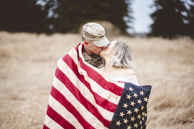 Free photo american soldier kissing his loving wife while wrapped in an american flag