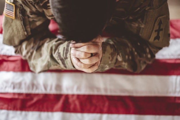 Free photo american soldier mourning and praying with the american flag in front of him