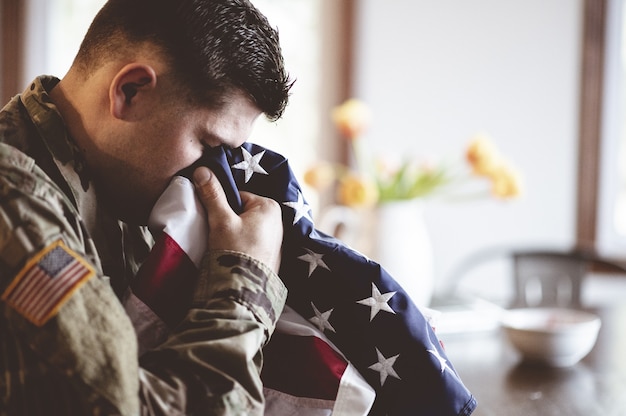 Free photo american soldier mourning and praying with the american flag in his hands